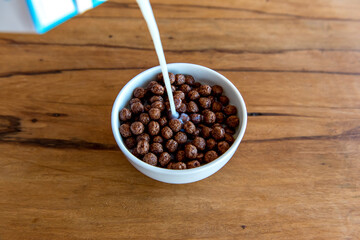 Pouring milk into chocolate cornflakes balls Breakfast with milk and cornflakes.