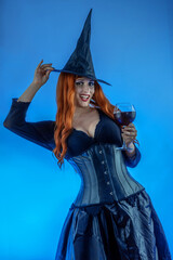 Halloween Witch Woman with long red hair and holiday make-up drinking potion cocktail or wine