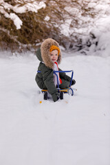 Little boy in warm winter overalls in winter in a park covered with snow