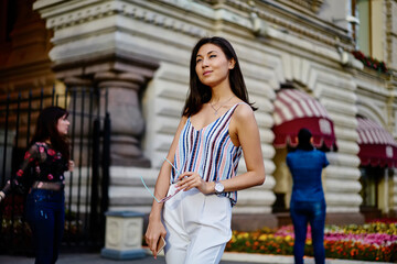 Contemplative hipster girl with sunglasses and modern cellphone technology thoughtful looking away and thinking about sightseeing excursion in touristic city,Asian female traveller pondering at street