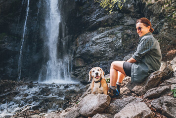 Smiling Female dog owner and his friend beagle dog resting near the mountain river waterfall during...