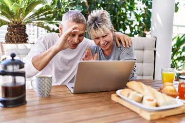 Senior caucasian couple having breakfast and video call using laptop at the terrace.