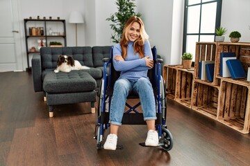 Young beautiful woman sitting on wheelchair at home happy face smiling with crossed arms looking at the camera. positive person.