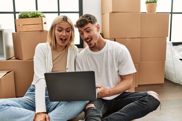 Young caucasian couple surprised using laptop sitting at new home.