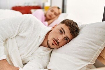 Young caucasian couple lying on the bed. Man looking to the camera at home.