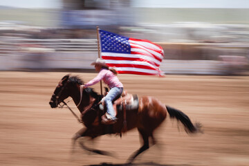 Cowgirl rides in rodeo with American flag. Motion blur Galisteo, New Mexico, United States.
