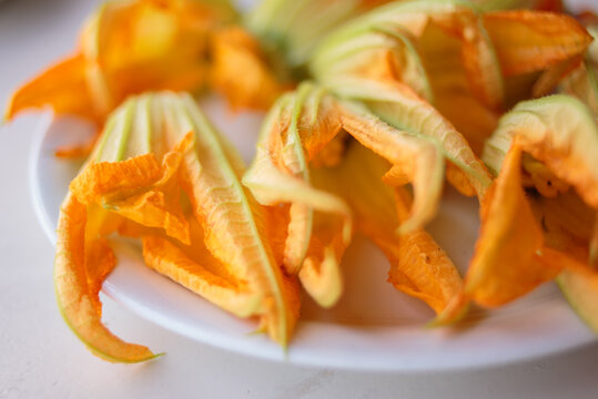 Zucchini flowers or courgette flowers on a white plate background. over white wooden table.  Organic food.