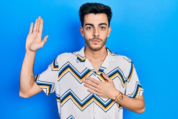 Young hispanic man wearing casual clothes swearing with hand on chest and open palm, making a...