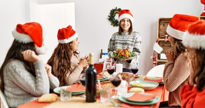 Group of hispanic women clapping and sitting on the table. Woman standing and holding roasted turkey celebrating Christmas at home.