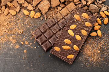 Cooking chocolate bars with almonds, desserts, handmade sweets. Composition of bars and pieces milk and dark chocolate, grated cocoa on black background top view. Confectionery craft on table