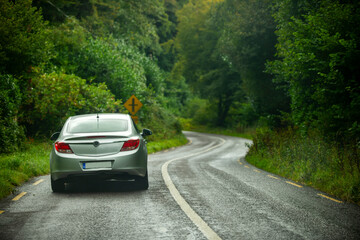 Modern gray vehicle driving on an Irish tree lined road on a typical country rainy day