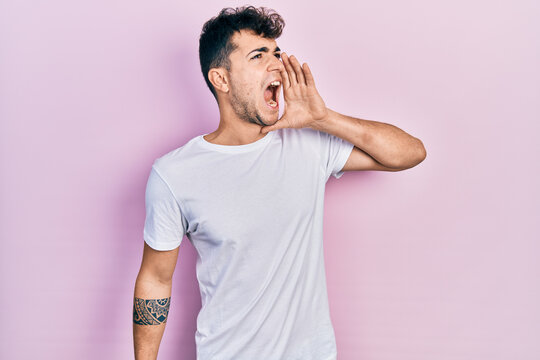 Young hispanic man wearing casual white t shirt shouting and screaming loud to side with hand on mouth. communication concept.