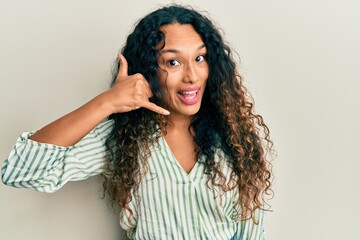 Young latin woman wearing casual clothes smiling doing phone gesture with hand and fingers like talking on the telephone. communicating concepts.