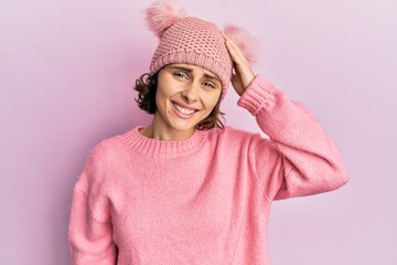 Young brunette woman wearing cute wool cap confuse and wonder about question. uncertain with doubt, thinking with hand on head. pensive concept.