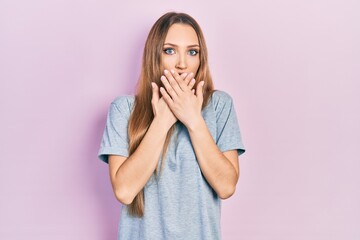 Young blonde girl wearing casual t shirt shocked covering mouth with hands for mistake. secret concept.