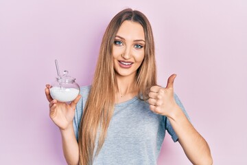 Young blonde girl holding bowl with sugar smiling happy and positive, thumb up doing excellent and...