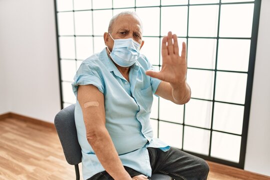 Mature Hispanic Man With Grey Hair Getting Vaccinated With Open Hand Doing Stop Sign With Serious And Confident Expression, Defense Gesture