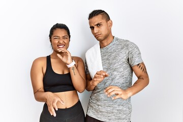 Young latin couple wearing sportswear standing over isolated background disgusted expression, displeased and fearful doing disgust face because aversion reaction. with hands raised