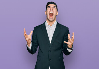 Handsome hispanic man wearing business clothes crazy and mad shouting and yelling with aggressive expression and arms raised. frustration concept.