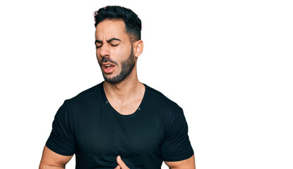 Hispanic man with beard wearing casual black t shirt with hand on stomach because nausea, painful disease feeling unwell. ache concept.