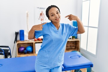 Young african american woman working at pain recovery clinic smiling cheerful showing and pointing with fingers teeth and mouth. dental health concept.
