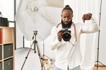 African american photographer man working at photography studio pointing down looking sad and upset, indicating direction with fingers, unhappy and depressed.