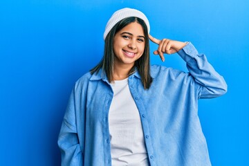 Young latin woman wearing cute wool cap smiling pointing to head with one finger, great idea or thought, good memory