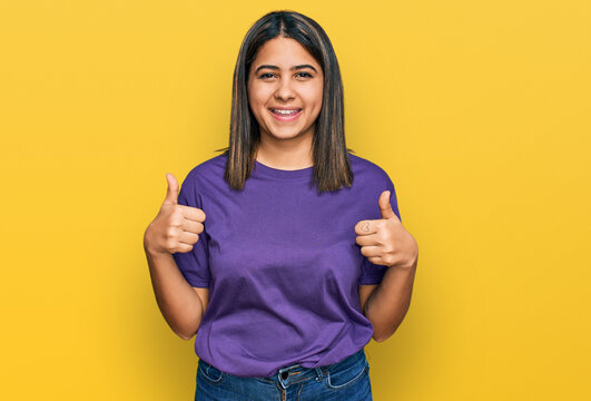 Young hispanic girl wearing casual purple t shirt success sign doing positive gesture with hand, thumbs up smiling and happy. cheerful expression and winner gesture.
