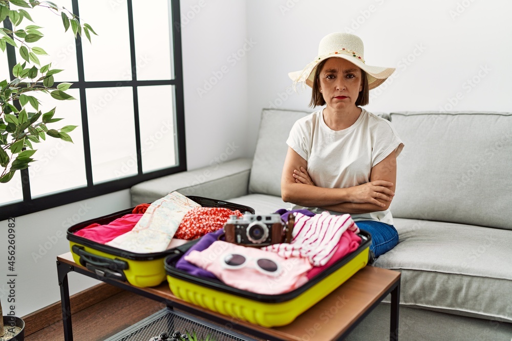 Wall mural beautiful middle age hispanic woman packing summer clothes in suitcase skeptic and nervous, disappro