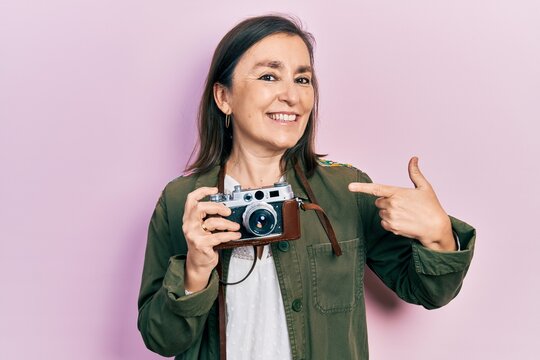 Middle age hispanic woman holding vintage camera smiling happy pointing with hand and finger