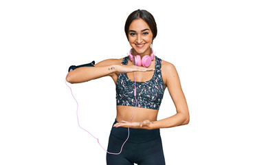 Beautiful brunette woman wearing gym clothes and using headphones gesturing with hands showing big and large size sign, measure symbol. smiling looking at the camera. measuring concept.