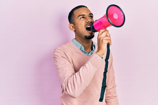 Young african american man shouthing and screaming through megaphone over pink isolated background