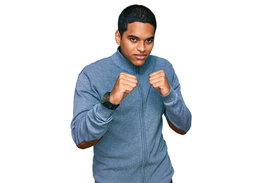 Young handsome hispanic man wearing casual sweatshirt ready to fight with fist defense gesture, angry and upset face, afraid of problem