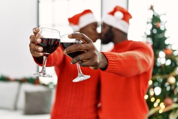 Young african american couple kissing and toasting with wine standing by christmas tree at home.