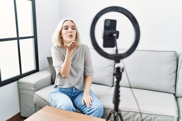 Young caucasian woman recording vlog tutorial with smartphone at home looking at the camera blowing a kiss with hand on air being lovely and sexy. love expression.