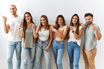 Obraz premium Group of young friends standing together over isolated background with a big smile on face, pointing with hand finger to the side looking at the camera.