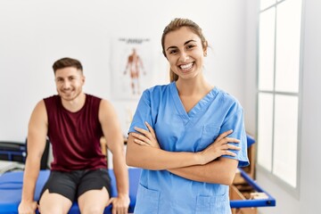 Fototapeta premium Young hispanic physioterapist woman smiling happy standing with arms crossed gesture at the clinic