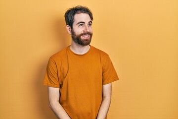 Caucasian man with beard wearing casual yellow t shirt smiling looking to the side and staring away thinking.