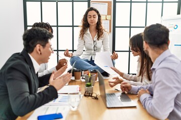 Fototapeta premium Businesswoman enjoys meditating during meeting. Sitting on desk near arguing partners at the office.