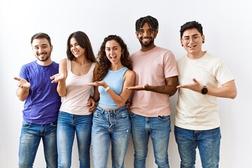 Obraz premium Group of young people standing together over isolated background pointing aside with hands open palms showing copy space, presenting advertisement smiling excited happy