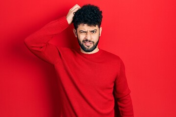 Young arab man with beard wearing casual red sweater confuse and wonder about question. uncertain...