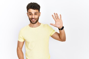 Arab young man standing over isolated background showing and pointing up with fingers number five while smiling confident and happy.