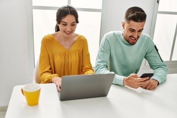 Young hispanic couple using laptop and smartphone drinking coffee at home.