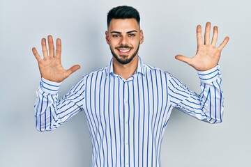 Young hispanic man with beard wearing casual striped shirt showing and pointing up with fingers number ten while smiling confident and happy.