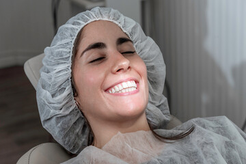 Mujer joven abre su boca con una sonrisa para ser atendida por el odontólogo y usa una gorra...
