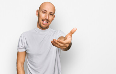 Fototapeta premium Bald man with beard wearing casual white t shirt smiling friendly offering handshake as greeting and welcoming. successful business.