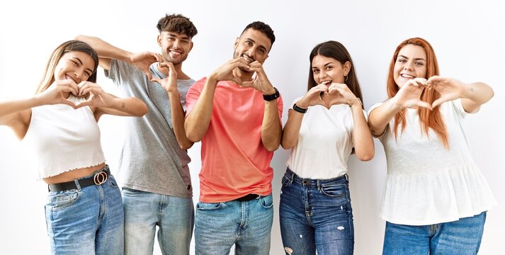 Group of young friends standing together over isolated background smiling in love doing heart symbol shape with hands. romantic concept.