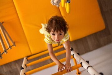 A little girl climbs the yellow sports complex with stairs and rings. The child leads a healthy...
