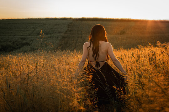 sunset, on a wheat field a young, beautiful, emotional girl - a brunette with long hair turned her back and goes to the sun. Peace, joy, nature, black and white photo