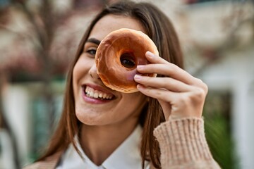 Young hispanic businesswoman smiling happy holding doughnut over eye at the city.